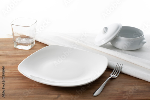 Menaje de comida plato, cuenco de sopa, vaso y cubiertos sobre tabla de madera. Dinnerware plate, soup bowl, glass and cutlery on wooden table.