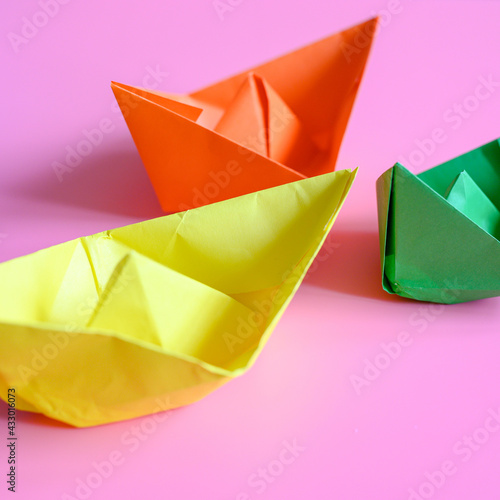 three bright colorful multicolor paper origami boats in orange  yellow and green colors on a pink background. square