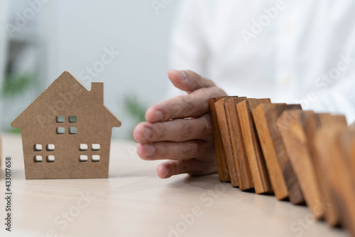 insurance with hands protect a house. The wooden domino block is about to fall on the house. Home insurance or house insurance concept