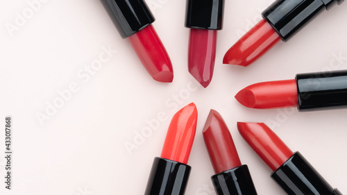 Red lipsticks of different shades arranged in a circle on beige background. Makeup and cosmetics concept. Close up. Flat layout. Copy space. photo