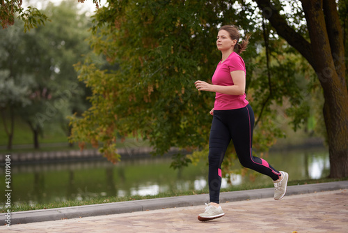 young woman in sportswear runs along in the park path