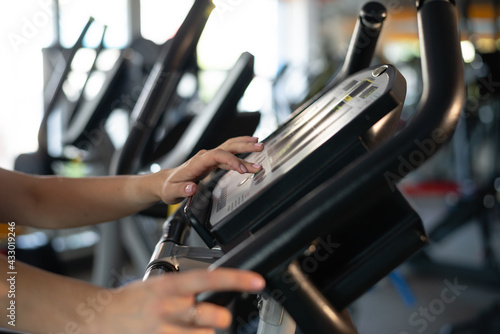 Female hands and monitor elliptical exercise control of a fitness tool on the background in the gym during a workout. Exercise bike or stepper.