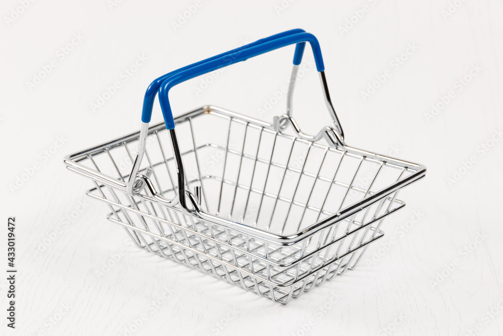 empty metal shiny basket with grocery handles on white wooden table background. close-up empty metal shiny basket with grocery handles on white wooden table background. close-up