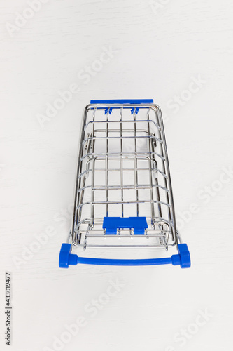 empty metal shiny grocery cart on wheels on white wooden table background