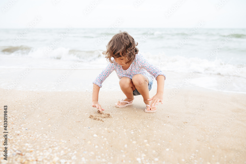 Five years cute curly caucasian girl painting on sand on the beach. Five years cute curly caucasian girl painting on sand on the beach.