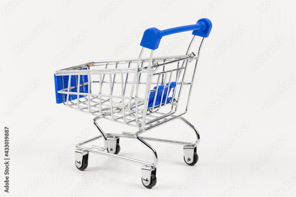 empty metal shiny grocery cart on wheels on white wooden table background empty metal shiny grocery cart on wheels on white wooden table background