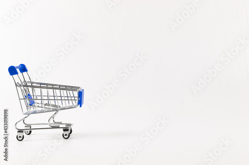 empty metal shiny grocery cart on wheels on white wooden table background