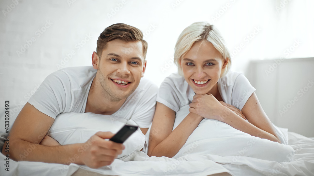 cheerful couple smiling while watching movie in bedroom cheerful couple smiling while watching movie in bedroom