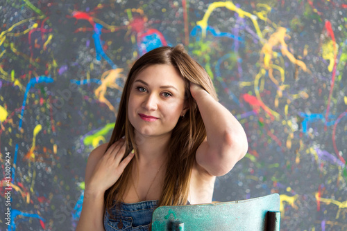 Portrait of a beautiful woman with dark hair, clean skin and natural makeup. Natural, beautiful smile. Woman is wearing a denim overalls. Used background using oil paints.