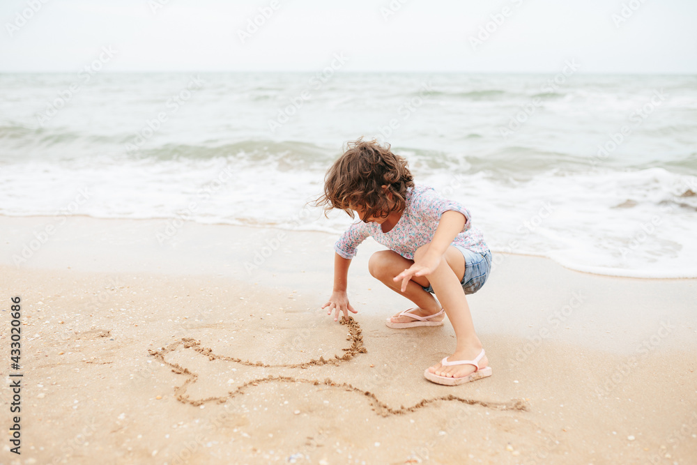 Five years cute curly caucasian girl painting on sand on the beach. Five years cute curly caucasian girl painting on sand on the beach.