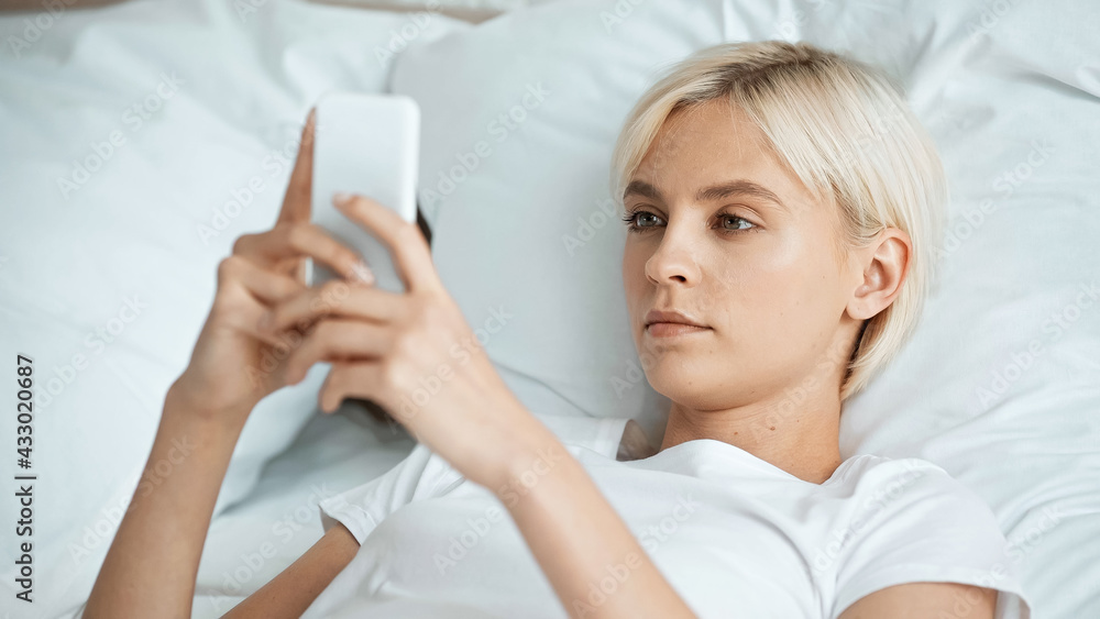 blonde young woman texting on smartphone in bedroom blonde young woman texting on smartphone in bedroom
