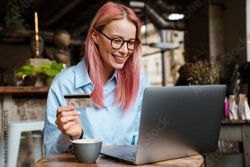 Young smiling woman using laptop and credit card while sitting in cafe