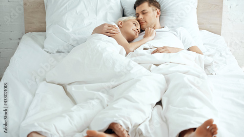 barefoot couple lying under blanket on bed