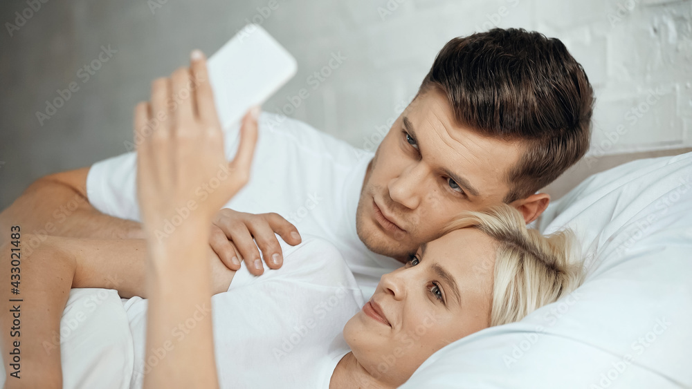 young man and joyful woman taking selfie on smartphone in bedroom young man and joyful woman taking selfie on smartphone in bedroom