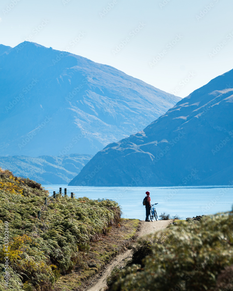 Cyclist standing with his bike enjoying the views of the Lake Wanaka on Glendhu Bay track, South Island. Vertical format