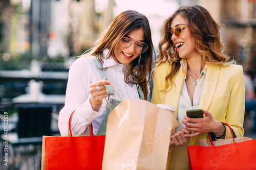 Two happy young women looking into shopping bags at the street