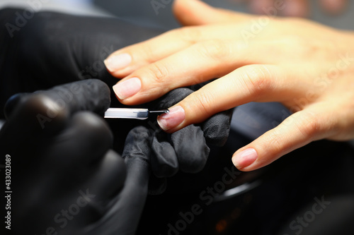 Master in rubber gloves painting client nails with transparent varnish closeup