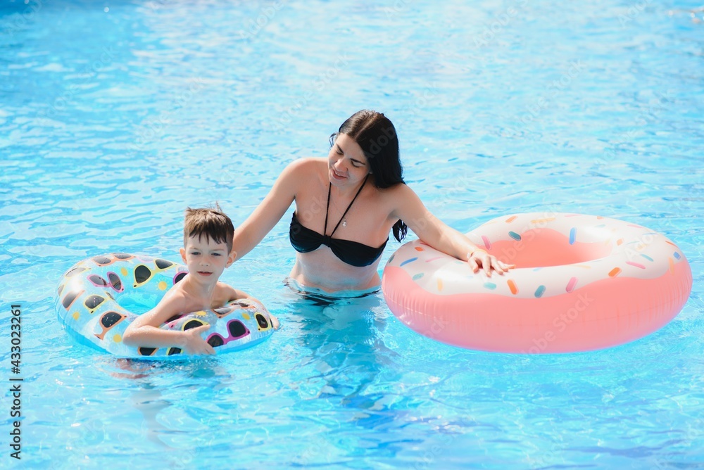 Mother and baby in outdoor swimming pool of tropical resort. Kid learning to swim. Mom and child playing in water. Family summer vacation in exotic destination. Active and healthy sport for kids.