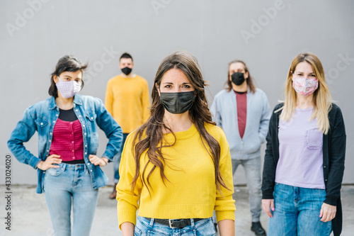 Portrait of a multiracial group of friends with masks in protection from Coronavirus infections, Covid-19 - Leader woman with other millennials behind her with serious eyes looking into camera smile
