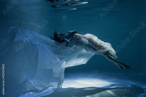 lighting on peaceful young woman in white elegant dress sleeping while swimming in pool