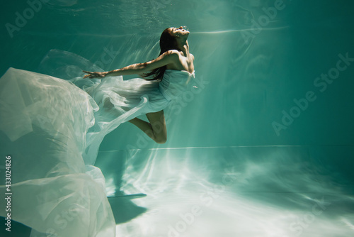 brunette young woman in dress diving in pool