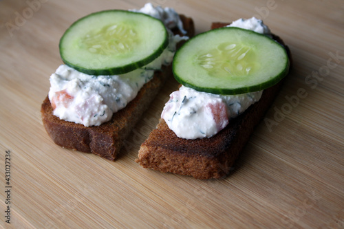 Cottage cheese dip with cucumber slices on black bread toast. Breakfast.