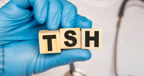 TSH Thyroid stimulating hormone - word from wooden blocks with letters holding by a doctor's hands in medical protective gloves. Medical concept. photo
