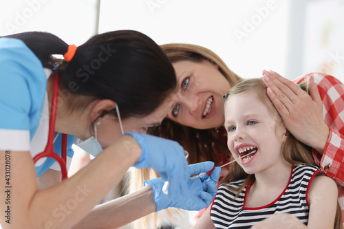 Doctor taking buccal dna swab from little girl in clinic