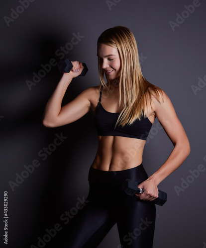 fitness blonde woman in the gym near the wall with dumbbells in her hands. © Ryzhkov Oleksandr