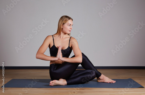 Young attractive woman practicing yoga, doing Half lord of the fishes exercise, Ardha Matsyendrasana pose with namaste