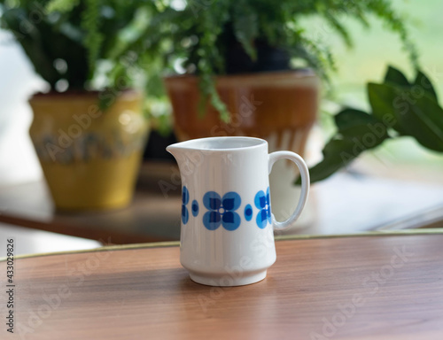 Mid-century modern cream pitcher on a wooden table before the window with plants