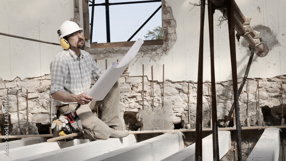 man at work, construction worker wearing helmet and looking at blueprint , check the house project plan, in renovation building site background with the beams at the base of the foundations man at work, construction worker wearing helmet and looking at blueprint , check the house project plan, in renovation building site background with the beams at the base of the foundations