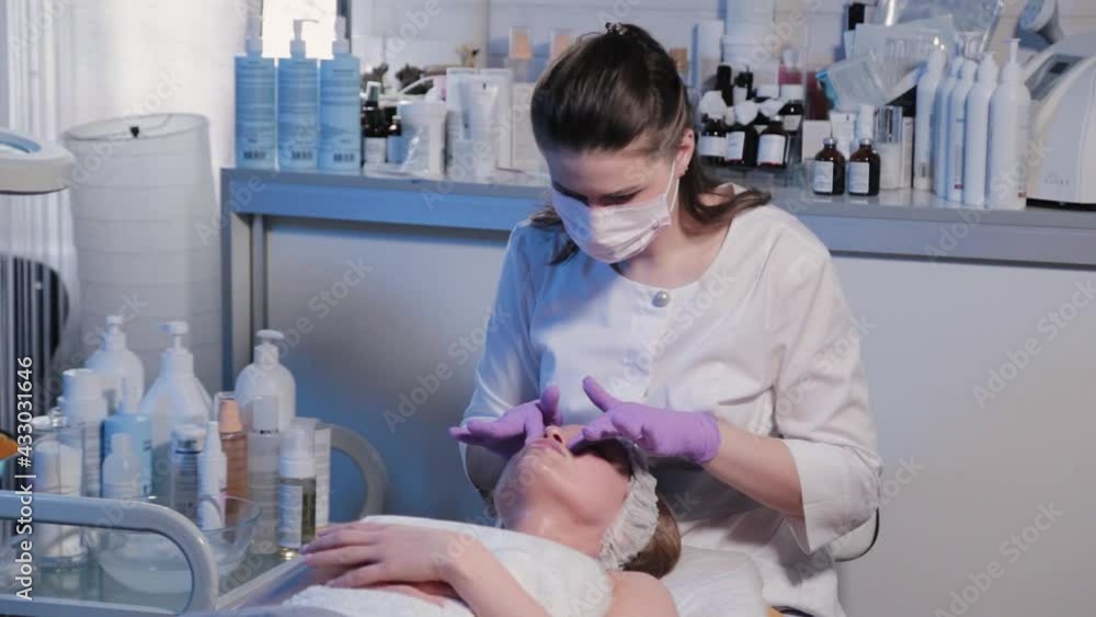 Woman beautician rubs cream on woman's face. Woman beautician rubs cream on woman's face.
