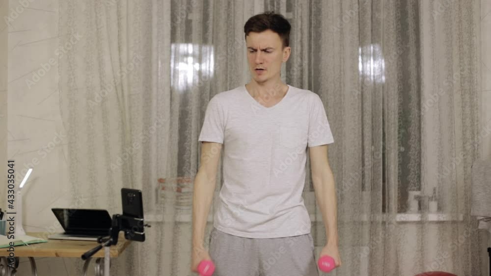 Slim funny man doing exercise with pink dumbbells during fitness workout at home Slim funny man doing exercise with pink dumbbells during fitness workout at home