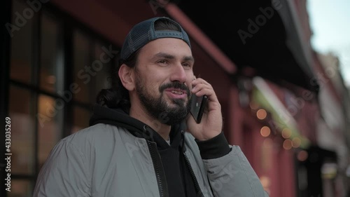 Young, modern handsome man talking on the phone on the street of a small town on a sunny spring day. photo