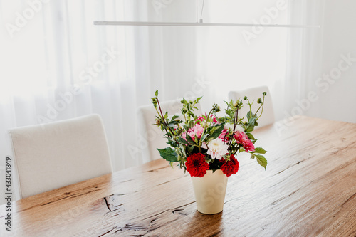 Dahlia flowers bouquet in a vase on wooden dining table. Modern room interior  bright and airy.