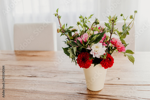 Dahlia flowers bouquet in a vase on wooden dining table. Modern room interior  bright and airy.