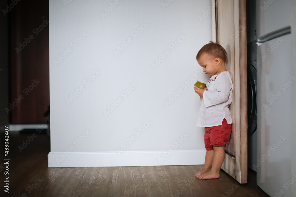 Cute baby Toddler eats tries green apple, little baby eats fruit on light background, lifestyle and cute kid, healthy eating