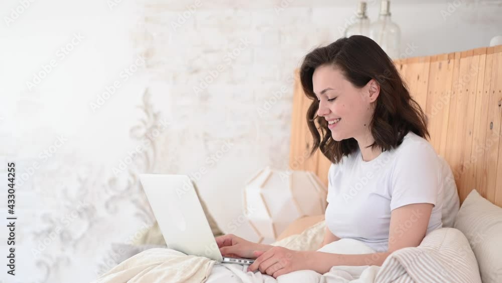 Woman Relaxing On Bed Using Laptop Computer For Video Call in modern flat Woman Relaxing On Bed Using Laptop Computer For Video Call in modern flat
