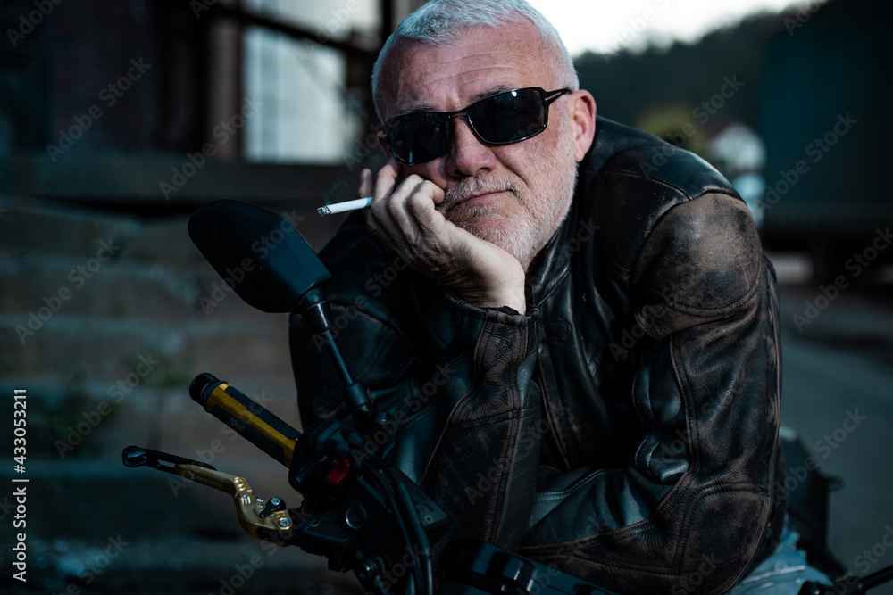 Portrait of an older man sitting on a bike while wearing a leather jacket.
