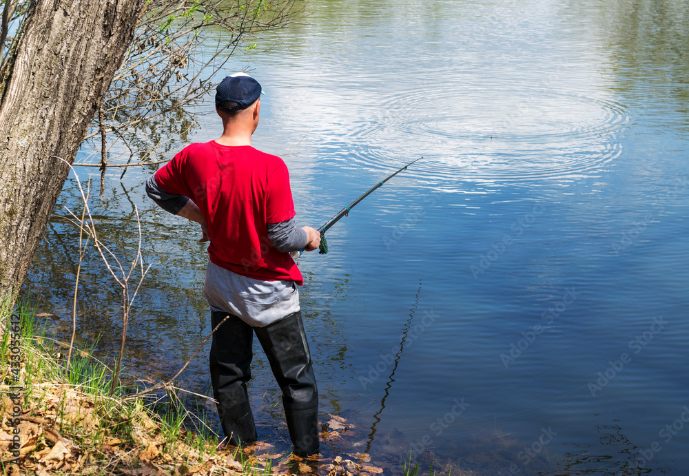 A man stands with a fishing rod on a lake and catches fish on a sunny summer day. A man stands with a fishing rod on a lake and catches fish on a sunny summer day.