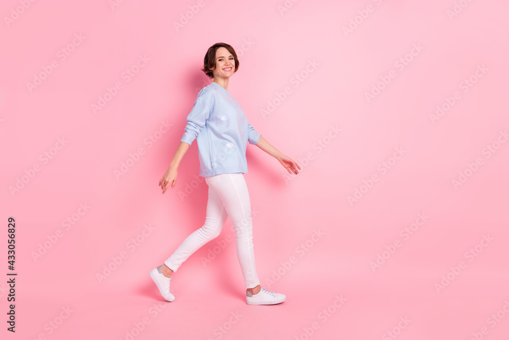 Full size profile side photo of young charming lovely positive girl go walk wear blue sweater isolated on pink color background Full size profile side photo of young charming lovely positive girl go walk wear blue sweater isolated on pink color background