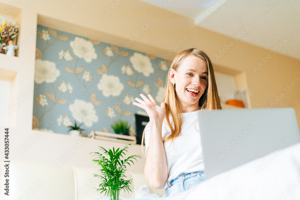 Blonde woman working at home office. Happy beautiful lady girl typing at laptop, having a video call chat, sits on bed with coffee cup. Using computer. Distance learning and online education. Blonde woman working at home office. Happy beautiful lady girl typing at laptop, having a video call chat, sits on bed with coffee cup. Using computer. Distance learning and online education.