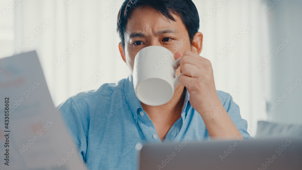Freelance Asia guy casual wear using laptop and drink coffee in living room at house. Working from home, remotely work, distance education, social distancing, quarantine for corona virus prevention. Freelance Asia guy casual wear using laptop and drink coffee in living room at house. Working from home, remotely work, distance education, social distancing, quarantine for corona virus prevention.