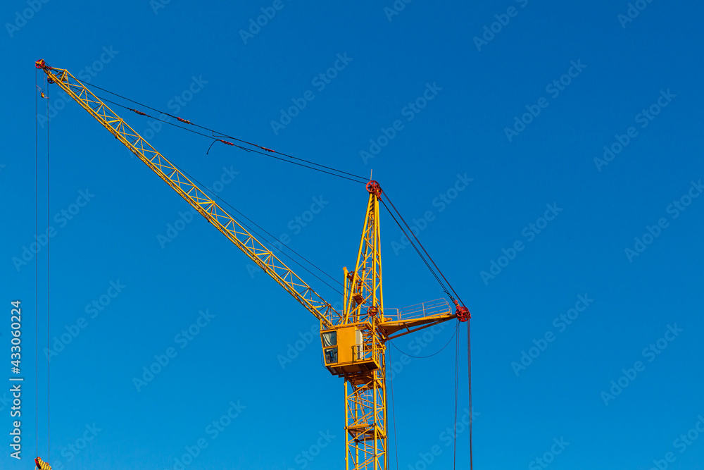 High yellow construction crane against the blue cloudless sky