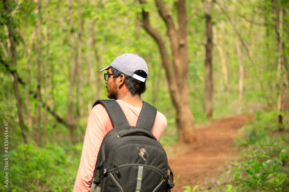 Backside view of a 18-25 year old Indian man adjusting his cap and a mask and walking freely in a jungle. Face towards the left side of the camera.