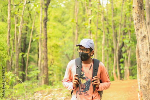 A 18-25 year old Indian man wearing a cap and a mask and walking freely in a jungle. Face towards the left side of the camera.