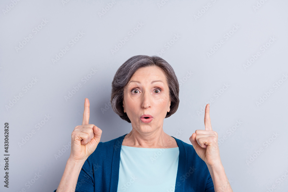 Photo of shocked impressed age woman wear blue cardigan pointing two fingers up empty space isolated green color background Photo of shocked impressed age woman wear blue cardigan pointing two fingers up empty space isolated green color background