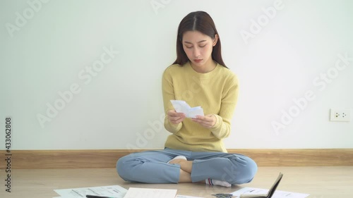 Front view owe asian woman, female sitting on floor stressed and confused by calculate expense from invoice or bill, have no money to pay, mortgage or loan. Debt, bankruptcy or bankrupt concept.