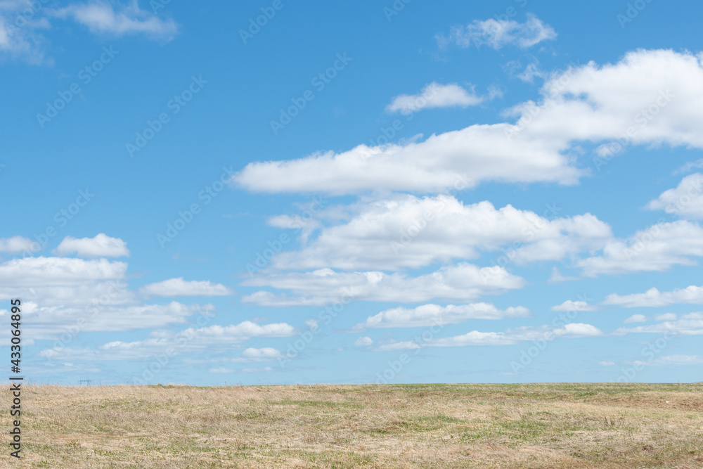 A bright blue sky meets rural barren tundra, parched earth. The peat moss is yellow and there's very little green grass on the land. The dry bare countryside has a steady incline to the rocky hill.